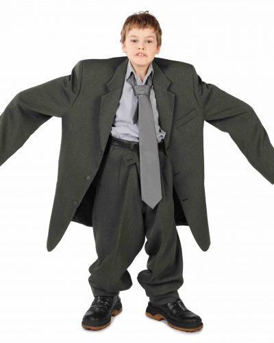 little boy in big grey man’s suit and boots nads at sides isolated on white background little boy in big grey man's suit and boots nads at sides isolated on white background